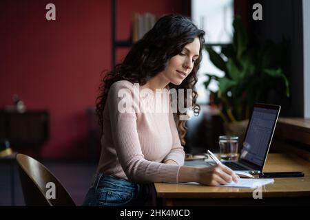 Une jeune femme d'affaires se prépare à la présentation du rapport financier et aux résultats des ventes. Notez-les dans le carnet Banque D'Images