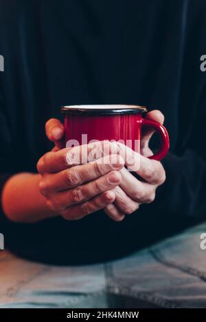 Gros plan des mains d'une femme tenant une tasse rouge avec un fond sombre pour le contenu promotionnel, le café, le chocolat ou le thé. Banque D'Images