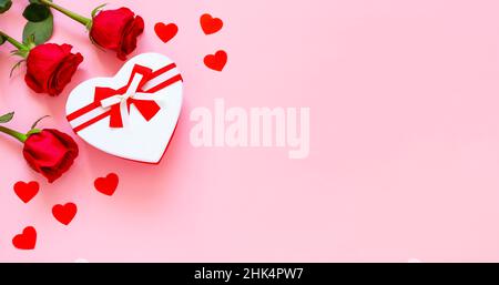 Roses rouges et boîte cadeau sur fond rose.Confession d'amour.Célébration de la Saint-Valentin.Boîte cadeau en forme de coeur avec ruban rouge et roses, concept de V Banque D'Images