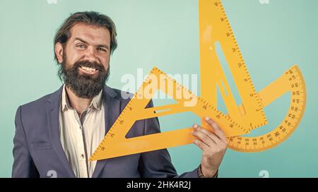 homme barbu mature enseignant en costume assis dans la classe d'école avec tableau noir, mesure Banque D'Images