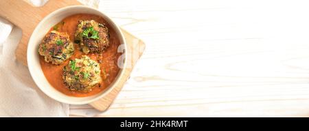 Boulettes de légumes frites de courgettes et de pommes de terre en sauce tomate sur un plan de cuisine et une table en bois clair, grand format panoramique avec espace de copie, haut Banque D'Images