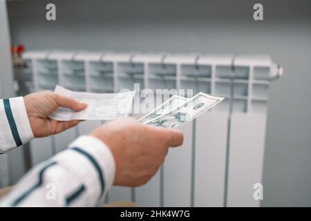 Des billets de dollars dans les mains des femmes près de la batterie de radiateur de chauffage à la maison.Frais de chauffage coûteux.Paiement des factures. Banque D'Images