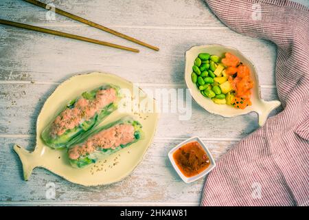 Deux petits pains d'été avec salade et saumon et sauce sur fond de bois blanc, cuisine japonaise et asiatique, vue de dessus Banque D'Images