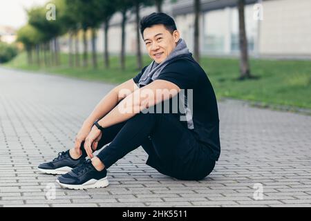 homme asiatique après l'entraînement de fitness et le jogging assis sur le sol fatigué de repos Banque D'Images