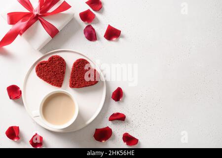 Gâteau de velours rouge en forme de cœur et café latte pour le petit déjeuner de la Saint-Valentin et cadeau sur fond blanc.Dessert savoureux.Vue de dessus. Banque D'Images