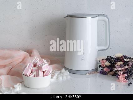 Sur le comptoir d'une cuisine guimauve lumineuse à côté d'une bouilloire électrique blanche et d'un bouquet de fleurs.Pause café. Banque D'Images