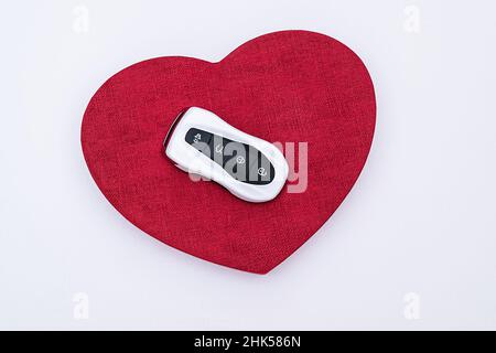 Concept Flat Lay et idée cadeau.Clé intelligente sur un coeur rouge en relief au milieu d'un fond blanc.Électronique, pièces de rechange et accessoires de voiture Banque D'Images