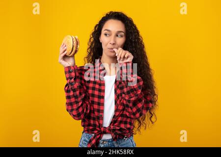 Happy Raughing Lady Eating Burger au Studio, lécher le doigt Banque D'Images