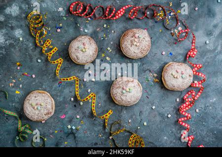 Krapfen, Berliner ou beignets avec banderoles, confetti et mini guimauves sur fond bleu.Image de carnaval ou d'anniversaire colorée, vue du dessus Banque D'Images