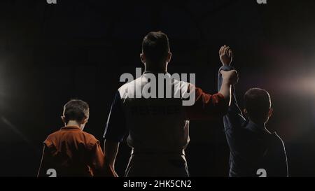 Vue arrière des garçons athlètes et arbitre qui lève la main du gagnant.L'arbitre lève la main du gagnant du garçon dans l'anneau.Judo. Banque D'Images