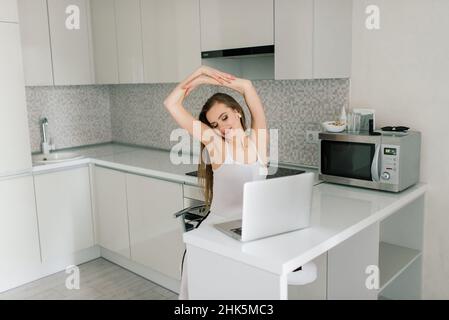 Femme en costume noir souriant à un ordinateur portable dans la cuisine Banque D'Images