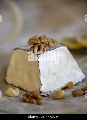 Fromage en moule blanc avec bords noirs de charbon de bois, noix et raisins secs, sur papier d'emballage.Production à domicile à partir de produits naturels. Banque D'Images