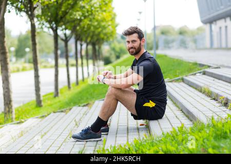Un athlète masculin réussi faisant de la forme physique le matin, se reposer et sourire se réjouit du résultat de l'entraînement dans le parc Banque D'Images