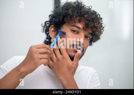 Jeune homme se raser le visage avant le miroir Banque D'Images