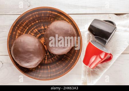 Deux beignets au chocolat doux sur un plat en céramique avec deux tasses sur une table en bois, vue macro, sur le dessus. Banque D'Images
