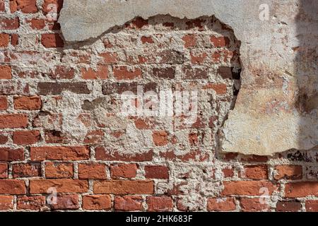 Fragment d'un mur de briques rouges partiellement recouvert de plâtre en fricleur pour une utilisation comme fond abstrait et texture. Banque D'Images