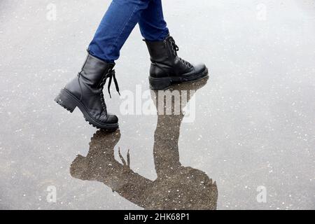 Reflet des jambes des femmes dans des bottes en cuir noir dans une flaque sur une rue.Pluie en ville, chaussures imperméables pour temps froid Banque D'Images