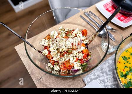 Salade grecque avec tomate et feta dans un bol en verre sur la table rempli de nourriture. Banque D'Images