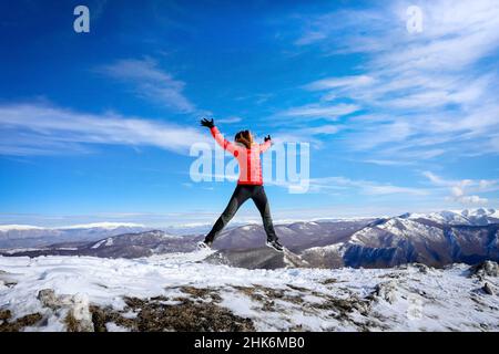 Randonneur au sommet de la montagne saute heureusement dans le ciel bleu en face de l'horizon des chaînes de montagnes Banque D'Images