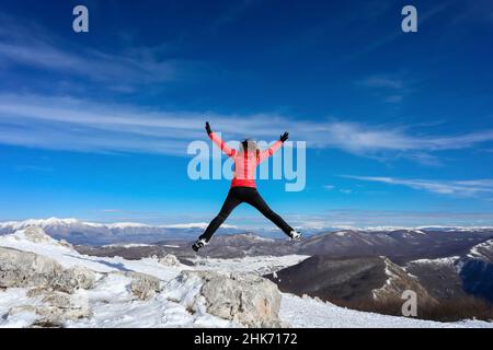Randonneur au sommet de la montagne saute heureusement dans le ciel bleu en face de l'horizon des chaînes de montagnes Banque D'Images
