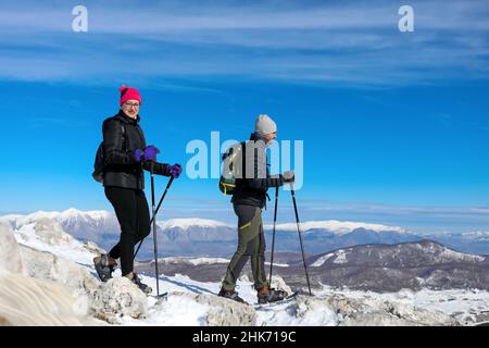 Deux randonneurs marchent avec des raquettes jusqu'au sommet enneigé, entouré d'un paysage immaculé et de chaînes de montagnes enneigées.Une belle journée d'hiver. Banque D'Images