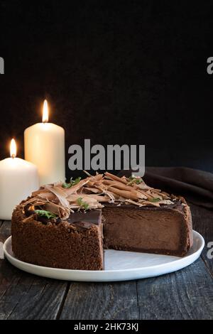 Cheesecake au chocolat ou gâteau éponge coupé sur une table en bois sombre aux chandelles. Encore la vie dans le style moodstyle. Banque D'Images