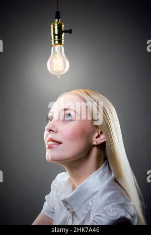 Jeune femme blonde contemple une ampoule Edison allumée Banque D'Images