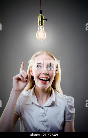 Jeune femme blonde, doigt pointant vers le haut sur l'ampoule Edison allumée Banque D'Images