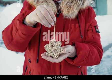 le chargeur fait de grains et de graisse est fait avec vos propres mains.Les mains des femmes tiennent un mangeoire à oiseaux.Protection et soutien des oiseaux dans le froid d'hiver. Banque D'Images