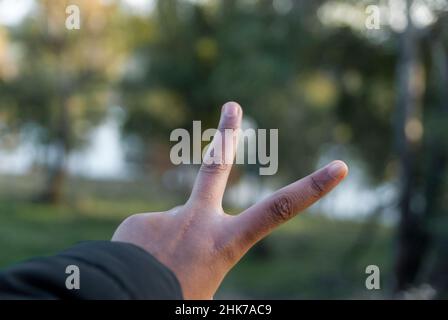 Signe de la victoire avec les doigts de la main avec un arrière-plan non focalisé et une zone pour le texte ou l'espace de copie Banque D'Images