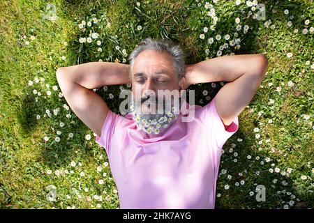 homme plus âgé avec une barbe décorée de fleurs couchée sur l'herbe un jour ensoleillé Banque D'Images