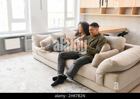 Divers jeunes conjoints utilisant leur smartphone, impliqués dans la navigation sur Internet.Couple multiracial heureux utilisant le téléphone tout en se relaxant Banque D'Images