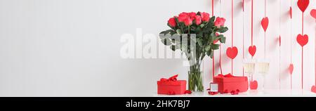 Bague d'engagement avec bouquet de fleurs, verres de champagne et cadeaux sur table près du mur lumineux dans la chambre Banque D'Images