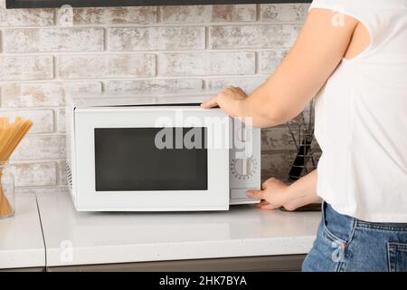 Femme utilisant un four à micro-ondes dans la cuisine Banque D'Images