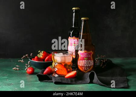 Bouteilles et verre de kombucha frais de fraise glacé sur fond sombre Banque D'Images