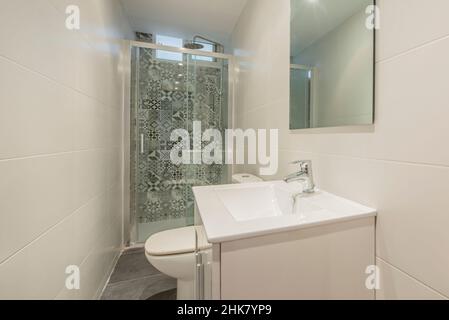 La salle de bains est décorée dans un style contemporain avec un mur de douche recouvert de carreaux hydrauliques, un meuble-lavabo blanc et un miroir en verre sans cadre Banque D'Images