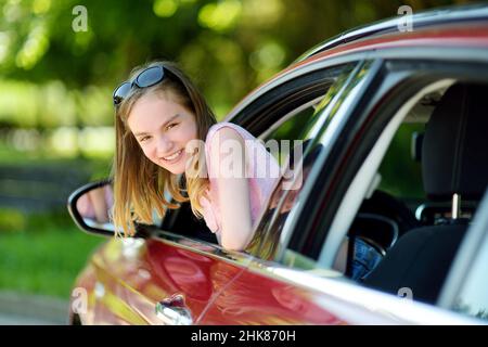 Jeune fille drôle de coller sa tête hors de la fenêtre de voiture regardant vers l'avant pour un voyage ou un voyage.Voiture familiale avec les enfants. Banque D'Images