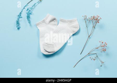 Paire de chaussettes blanches pour femmes et branches décoratives sur fond bleu, vue du dessus. Banque D'Images