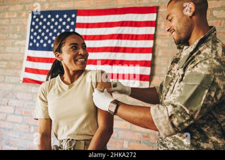 Une femme heureuse sourit à l'infirmière militaire après avoir reçu un rappel de vaccin Covid-19.Militaire américaine ayant un adhésif médical appliqué Banque D'Images