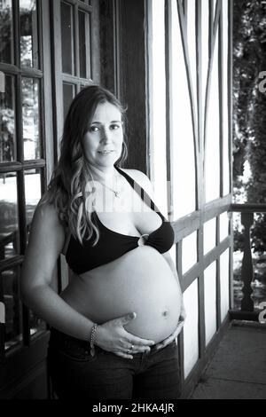 Jeune femme enceinte de sept mois vêtue de bikini noir et de jeans Banque D'Images