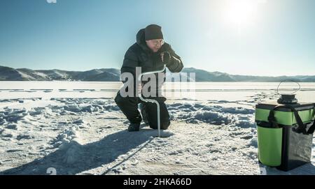 Un pêcheur fore un trou dans la glace d'un grand lac gelé par une journée ensoleillée.La joie de la pêche d'hiver Banque D'Images