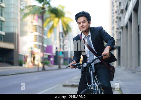 Un homme d'affaires asiatique en costume est à vélo dans les rues de la ville pour se rendre au travail le matin. Concept de transport écologique. Banque D'Images