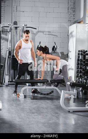 Moyen-Orient sportswoman s'entraîner avec haltères sur un banc plat près de l'entraîneur dans la salle de gym Banque D'Images