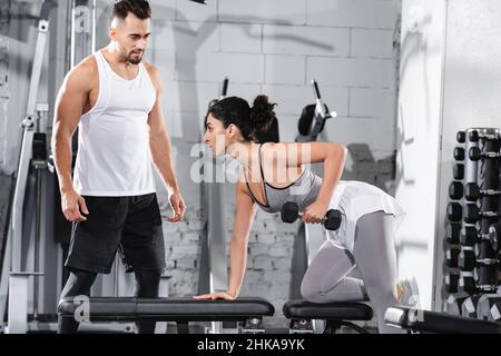 Entraîneur debout près du milieu est entraînement sportswoman avec haltères dans la salle de gym Banque D'Images