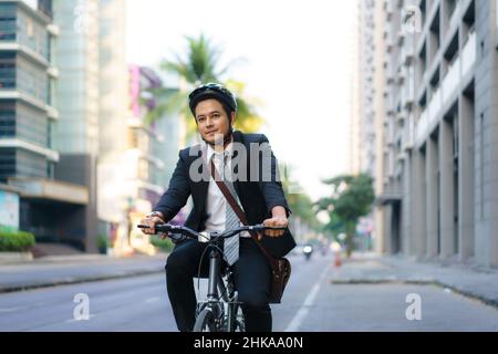 Un homme d'affaires asiatique en costume est à vélo dans les rues de la ville pour se rendre au travail le matin. Concept de transport écologique. Banque D'Images