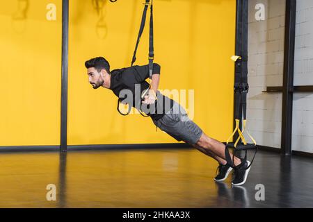 Vue latérale d'un sportif musulman qui s'efforce avec des sangles de suspension dans le centre sportif Banque D'Images