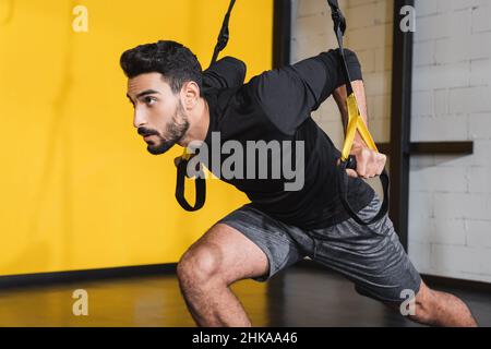 Sportif arabe barbu tirant des sangles de suspension dans la salle de sport Banque D'Images