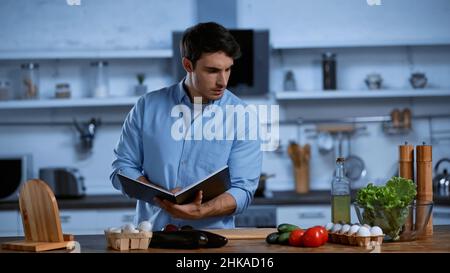 jeune homme tenant un livre de cuisine tout en regardant la table avec des ingrédients frais Banque D'Images