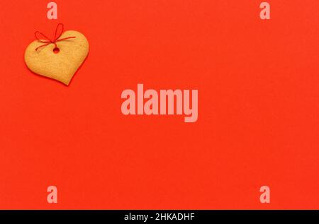 Biscuits au gingembre en forme de coeur, ornés d'un noeud sur fond rouge.Vue de dessus espace copie carte de Saint-Valentin. Banque D'Images