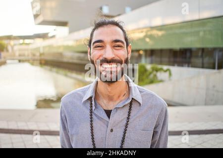 Portrait d'un jeune homme joyeux debout à l'extérieur et souriant à l'appareil photo.Bel homme heureux barbu.Concept d'émotion Banque D'Images